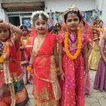 Group of young girls in vibrant traditional indian outfits with marigold garlands at a festival outside a building